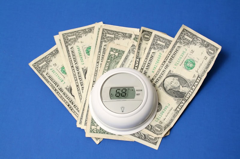 Spring Money-Saving Tips. Photo of a thermostat on top of a pile of dollar bills with a blue background.